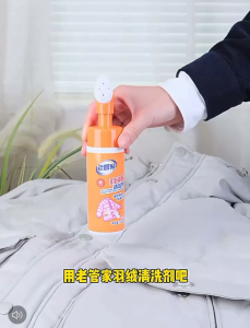 Orange foam bottle for down jackets. Removes stains effectively. No water cleaning required. Suitable for down jackets. Scene: hanging jackets.