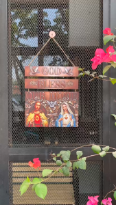 Wooden wall art with religious imagery and text "God Bless Our Home" in a home setting