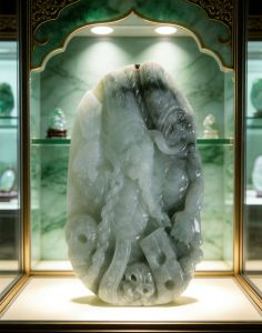 Jade carving with deity figure intricate details smooth texture green and white hues displayed in glass case.