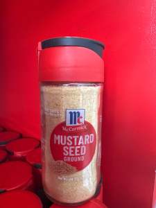 McCormick Mustard Seed Ground 26g Small Bottler Cooking & Seasoning - Red cap clear container visible mustard seeds red label with brand logo placed on red shelf.
