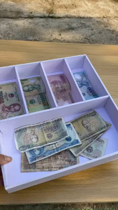 Hộp đựng tiền giấy 5 ngăn màu trắng với các mệnh giá khác nhau đặt trên bàn gỗ.