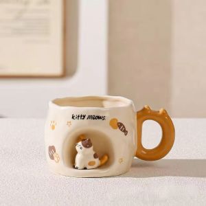 Ceramic mugs with cat figurines and paw prints black and brown handles "kitty meows" text on a book.