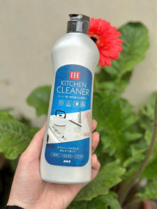 Nước rửa chén IH Kitchen Cleaner chai nhựa trắng nhãn xanh dương hình ảnh dụng cụ nhà bếp tay cầm chai nền cây xanh và hoa đỏ.