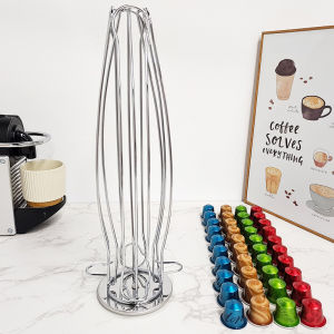 Stainless steel coffee pod holder with 24 capsules in assorted colors on marble countertop next to coffee machine and framed poster.