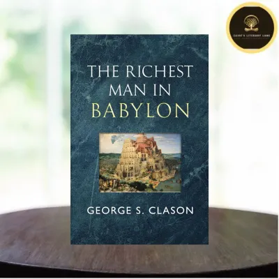 The Richest Man in Babylon by George S. Clason. Hardcover book with textured dark blue cover. Features an illustration of an ancient city. Displayed on a wooden surface near a window.