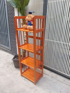 Kệ gỗ cao 4 tầng sâu 28 cm ngang 40cm cao 120 cmmàu nâu đỏ có gấu bông đội mũ tốt nghiệp trên kệ đặt ngoài trời cạnh chậu cây.