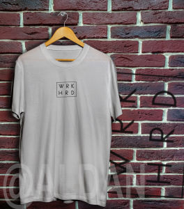 TIPIDSHOP black graphic t-shirt for men and women with "WRK HRD" text made of thick cotton hanging on wooden hanger against brick wall.