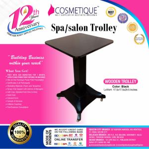 Black wooden spa/salon trolley with square top and four wheels. Dimensions: 17.5 x 17.5 x 29.5 inches.